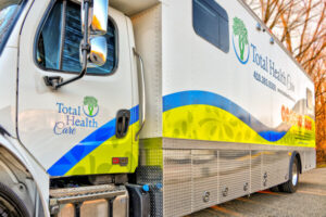 A Total Health Care mobile clinic truck, representing leading mobile health clinics, is parked on a road with the company logo and contact information displayed on its side.