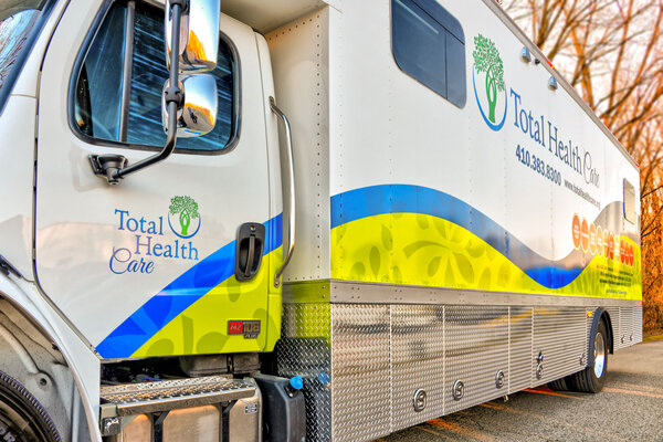 A Total Health Care mobile clinic truck, representing leading mobile health clinics, is parked on a road with the company logo and contact information displayed on its side.