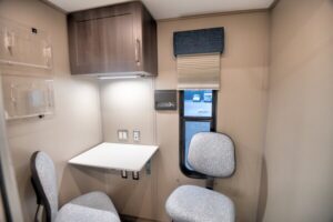 Small office space with two chairs, a wall-mounted desk, upper cabinet, power outlets, window with blinds, and a dispenser—ideal for CMS rural health investment initiatives seeking practical and efficient work environments.