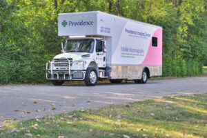 Providence Mobile Mammography truck parked on a paved road with trees and grass in the background, supporting community wellness alongside mobile behavioral health services.