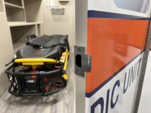 A stretcher is positioned in a room near an open door labeled 