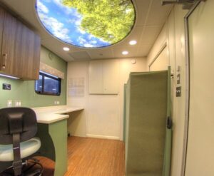 Interior of a modern office with a desk, chair, cabinetry, and a ceiling light that displays an image of trees and sky—an inspiring setting reminiscent of the innovative design often seen in mobile simulation laboratories.