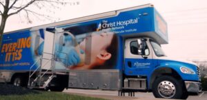 A mobile medical clinic vehicle branded with The Christ Hospital Health Network logo, shown as one of our mobile audiology clinics with an image of a patient receiving an ultrasound.